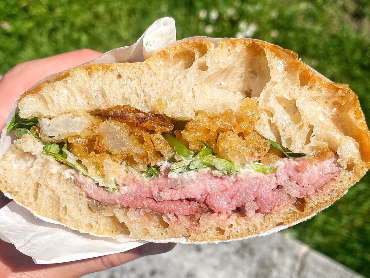 A cross-section of a sandwich, with focaccia, onion fritter, horseradish cream, peashoots, rare roast beef, and focaccia from top to bottom