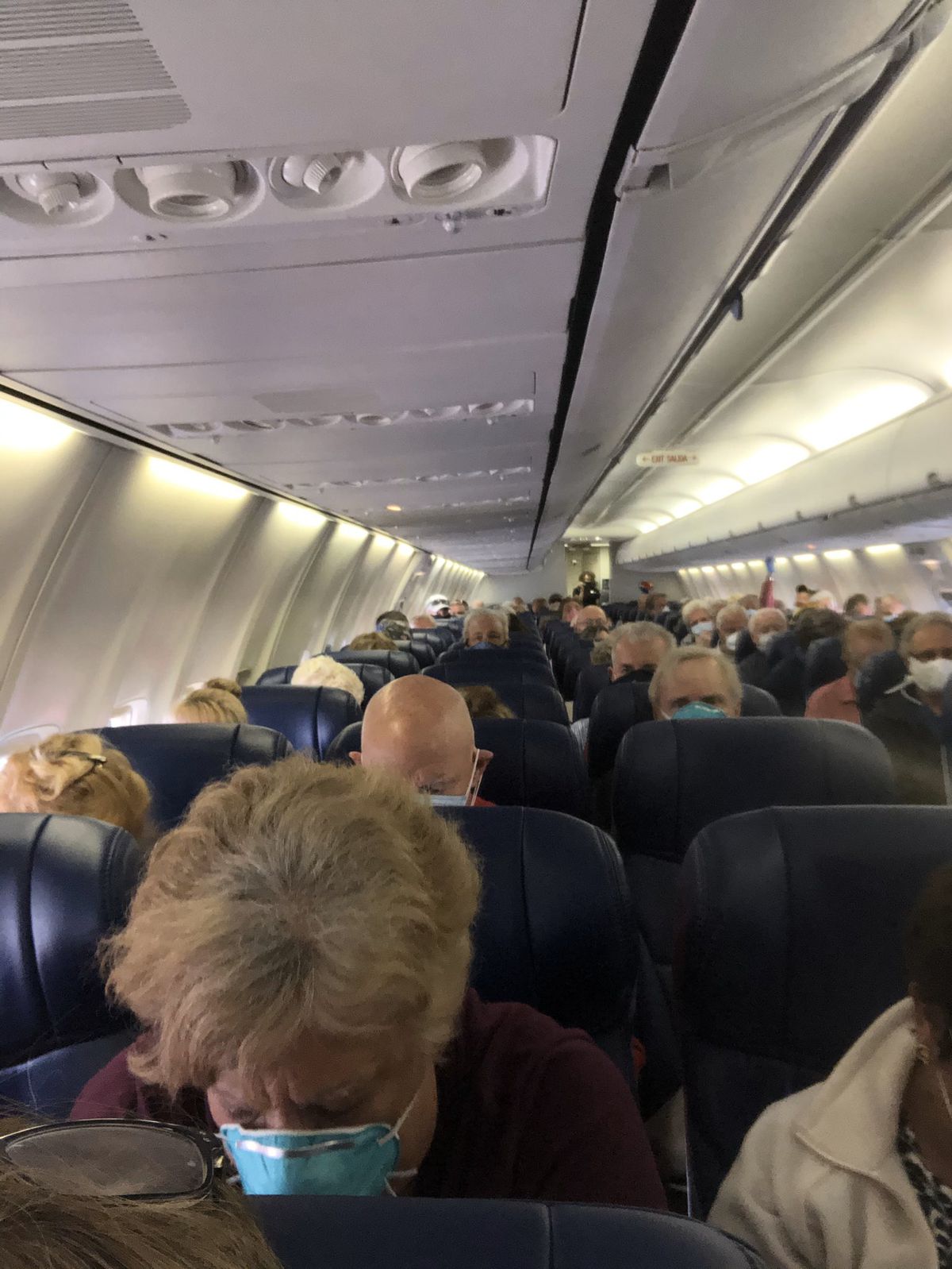 A crowded plane with elderly masked people.
