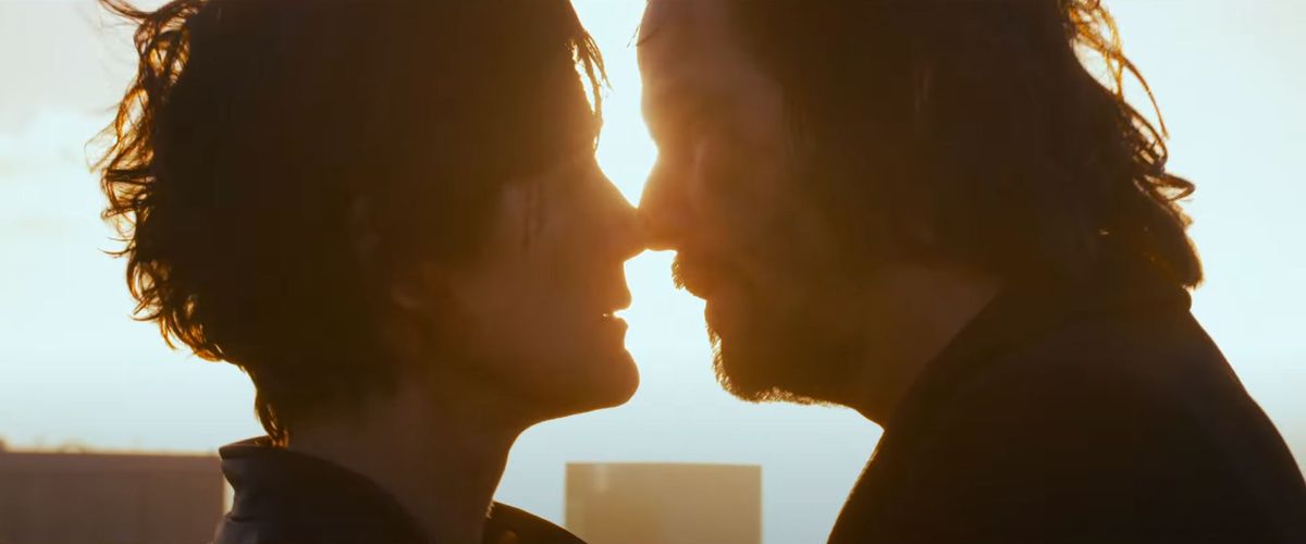 In this image from The Matrix Resurrections, Neo and Trinity lean towards one another for a kiss, while backlit by sunlight
