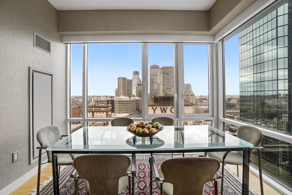 A dining room with a table and chairs as well as a floor-to-ceiling window overlooking a city.