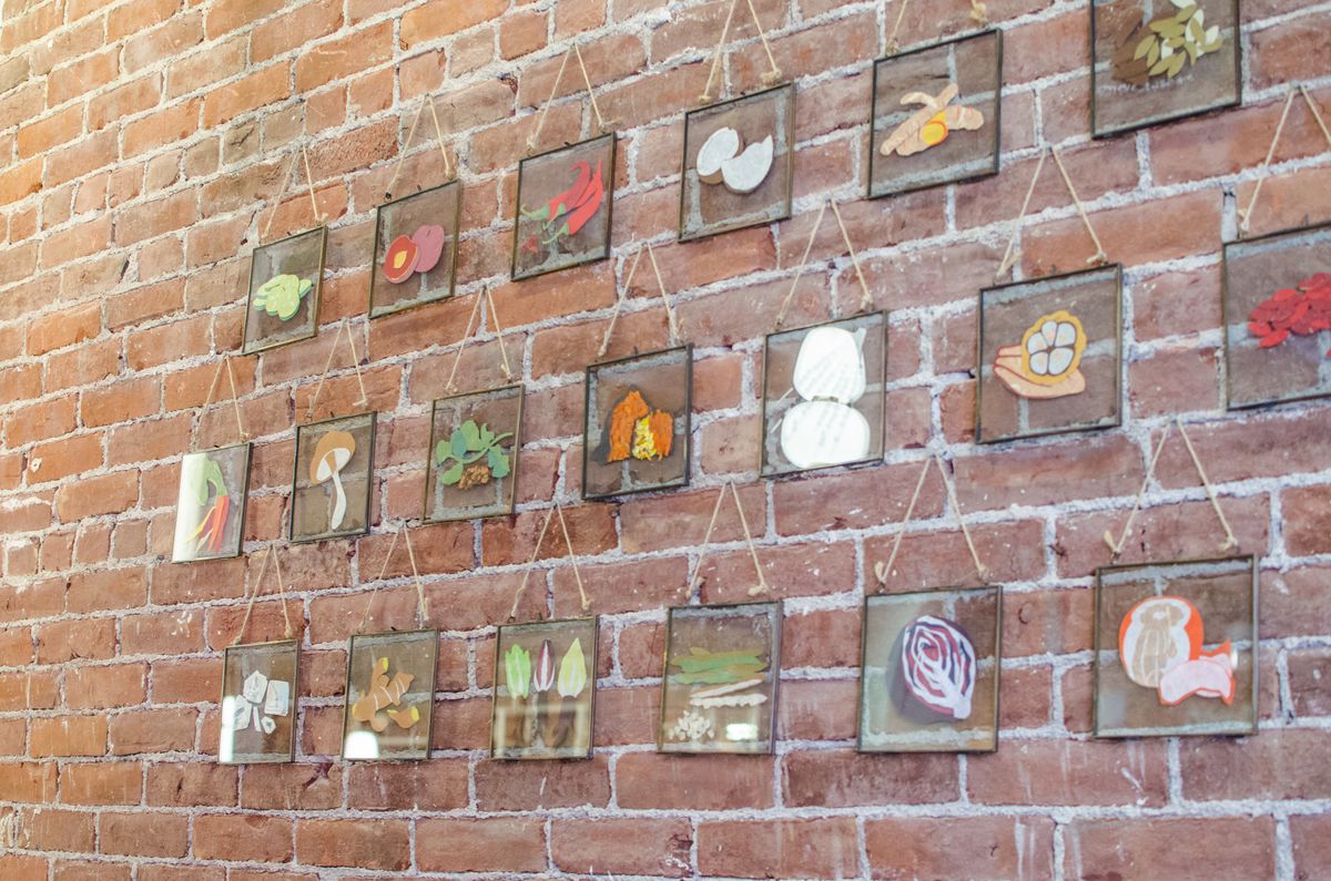 Small glass squares with different fruits and vegetables on them hang in a grid on a brick wall.