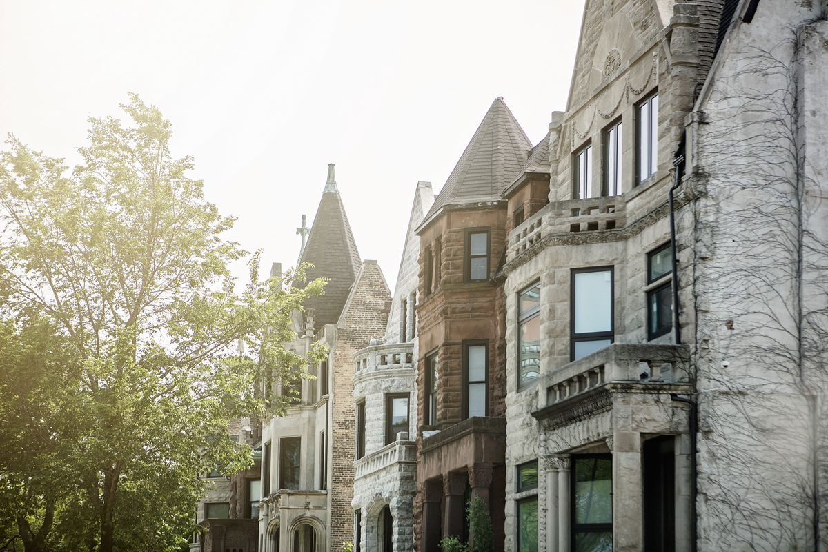 A row of Chicago homes with brick and greystone exteriors. There is a tree and clear sky.