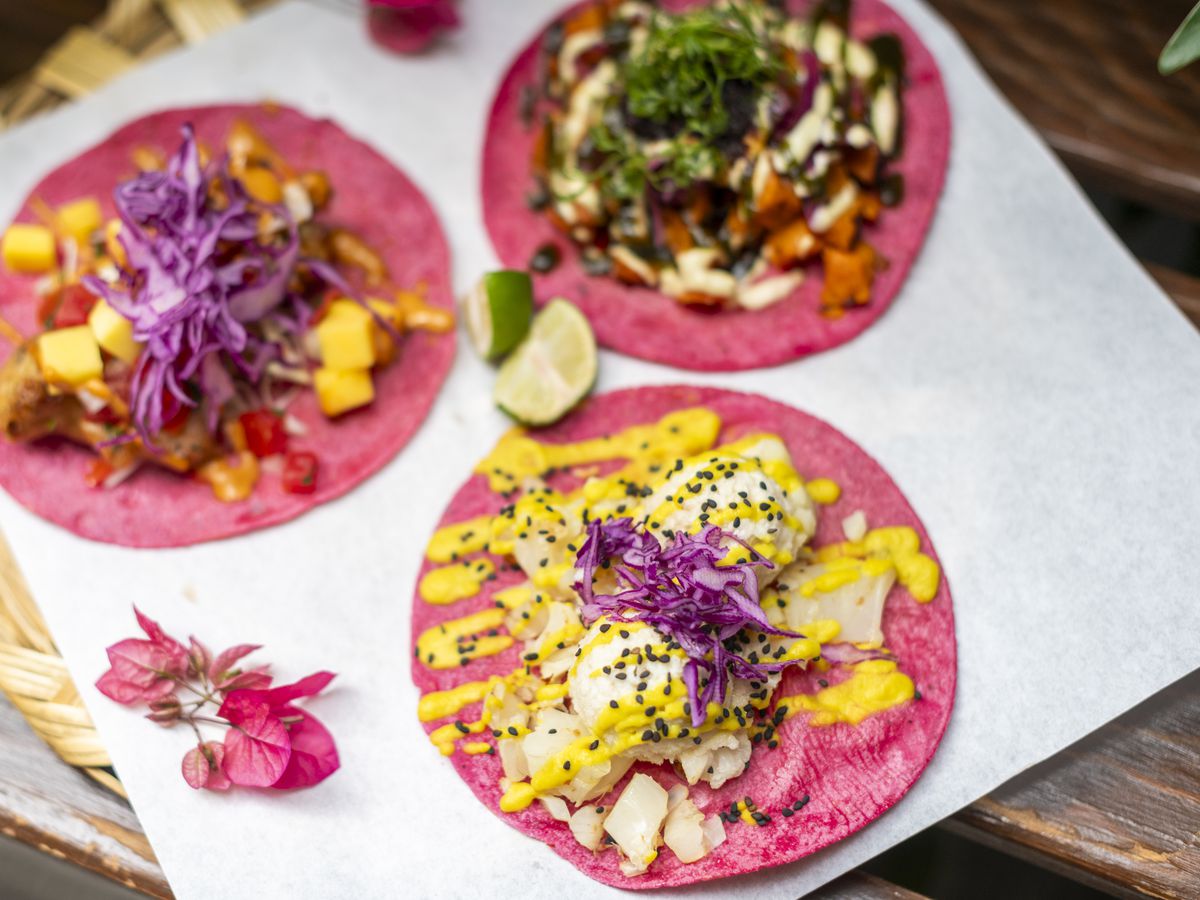 Three tacos with different colorful fillings on served on bright pink tortillas. 