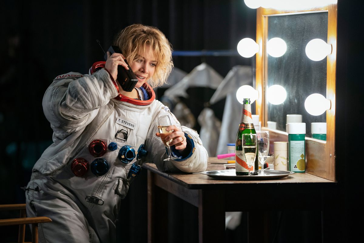 Sarah Jones in an astronaut flight suit talks on a giant mobile phone in front of a lighted makeup mirror in For All Mankind season 2