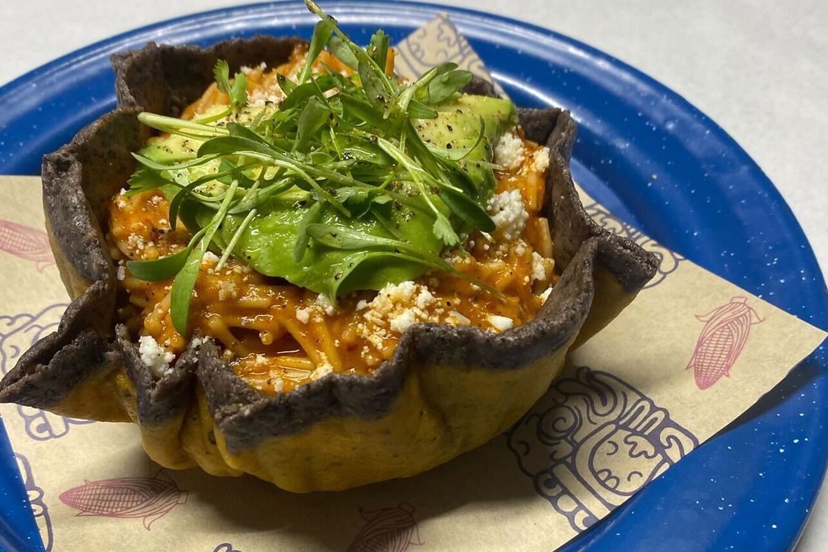 A blue taco bowl topped with microcilantro sitting on a blue plate with brown decorative paper.