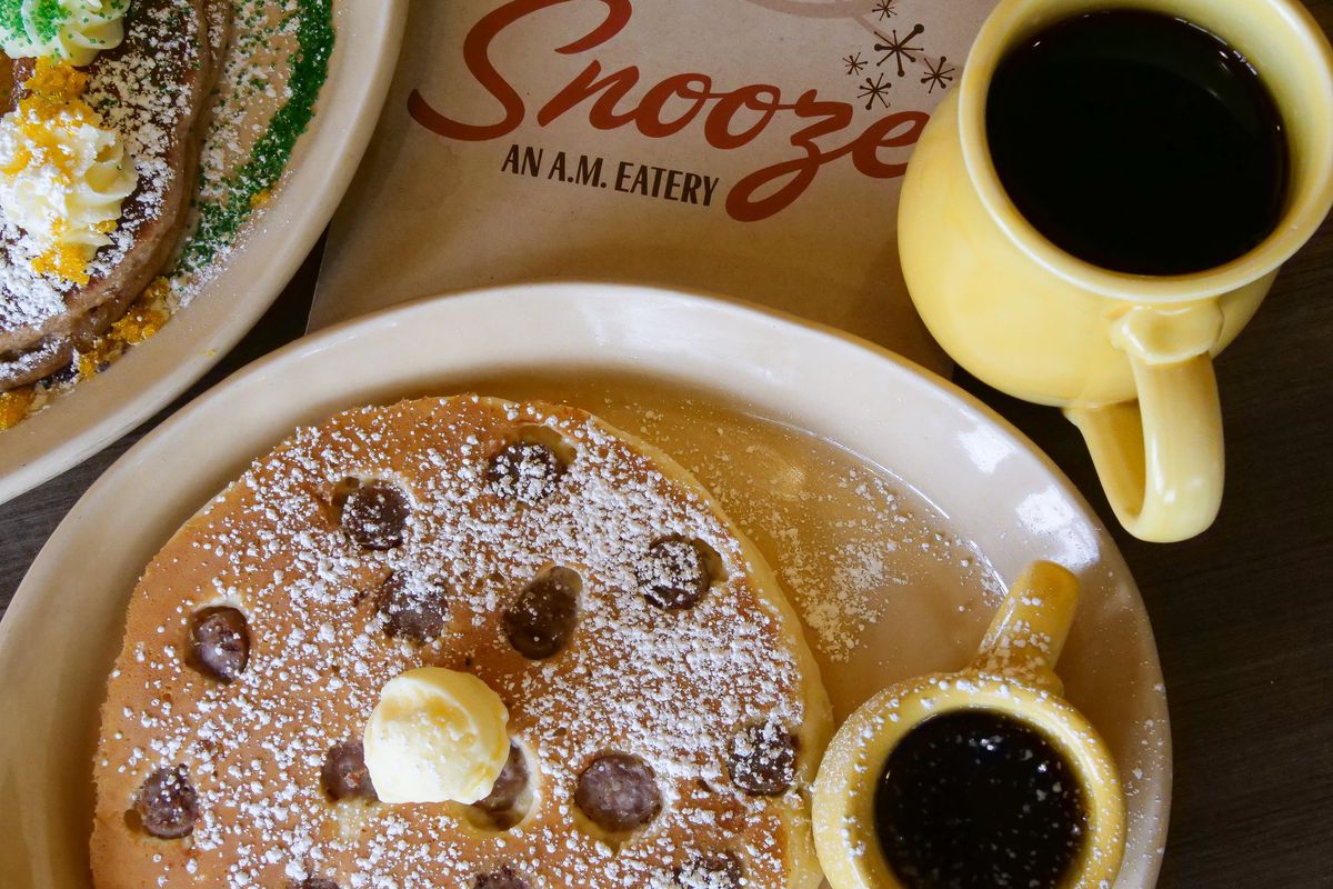 A close-up of a plate of pancakes with butter and syrup next to a cup of coffee at Snooze