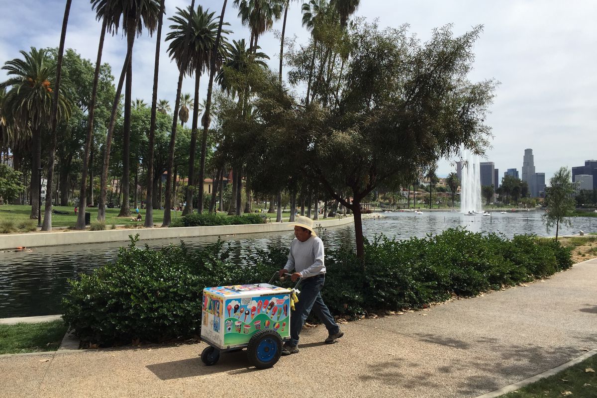 A vendor sells at Echo Park Lake on a sunny day, pushing a cart of paletas.