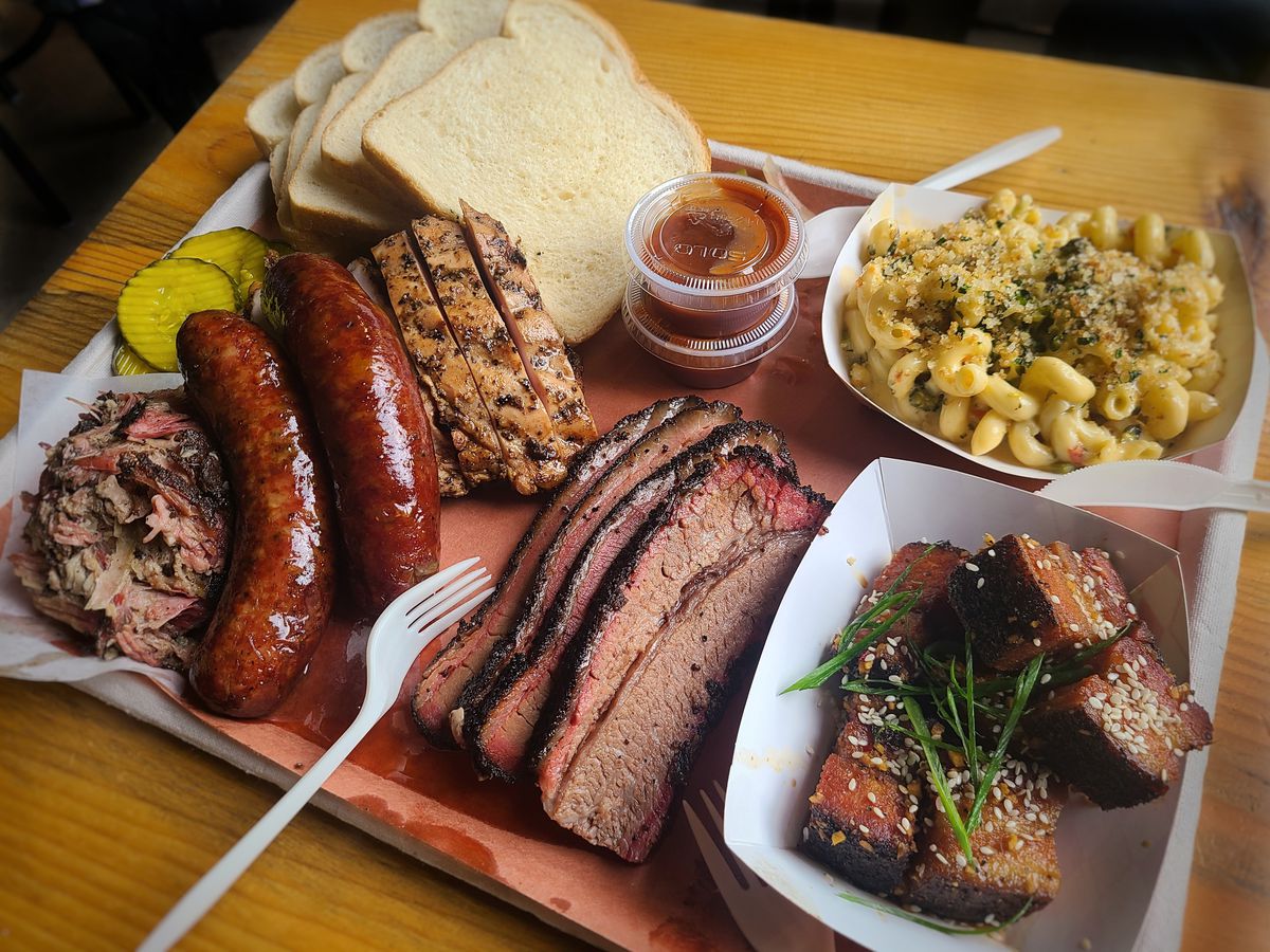 A selection of meats including sausage, brisket, and pork belly burnt ends are shown on a tray lined with butcher paper.
