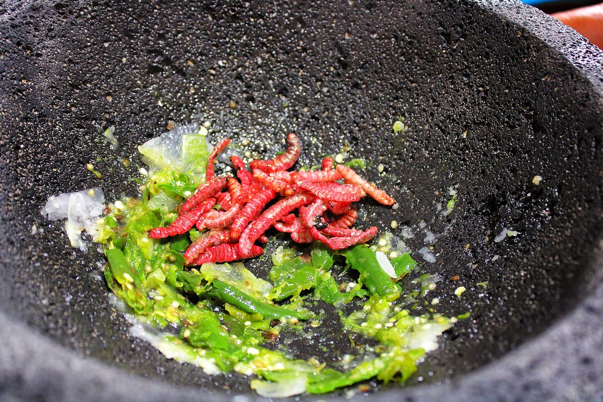 A pile of worms in a molcajete with crushed peppers. 