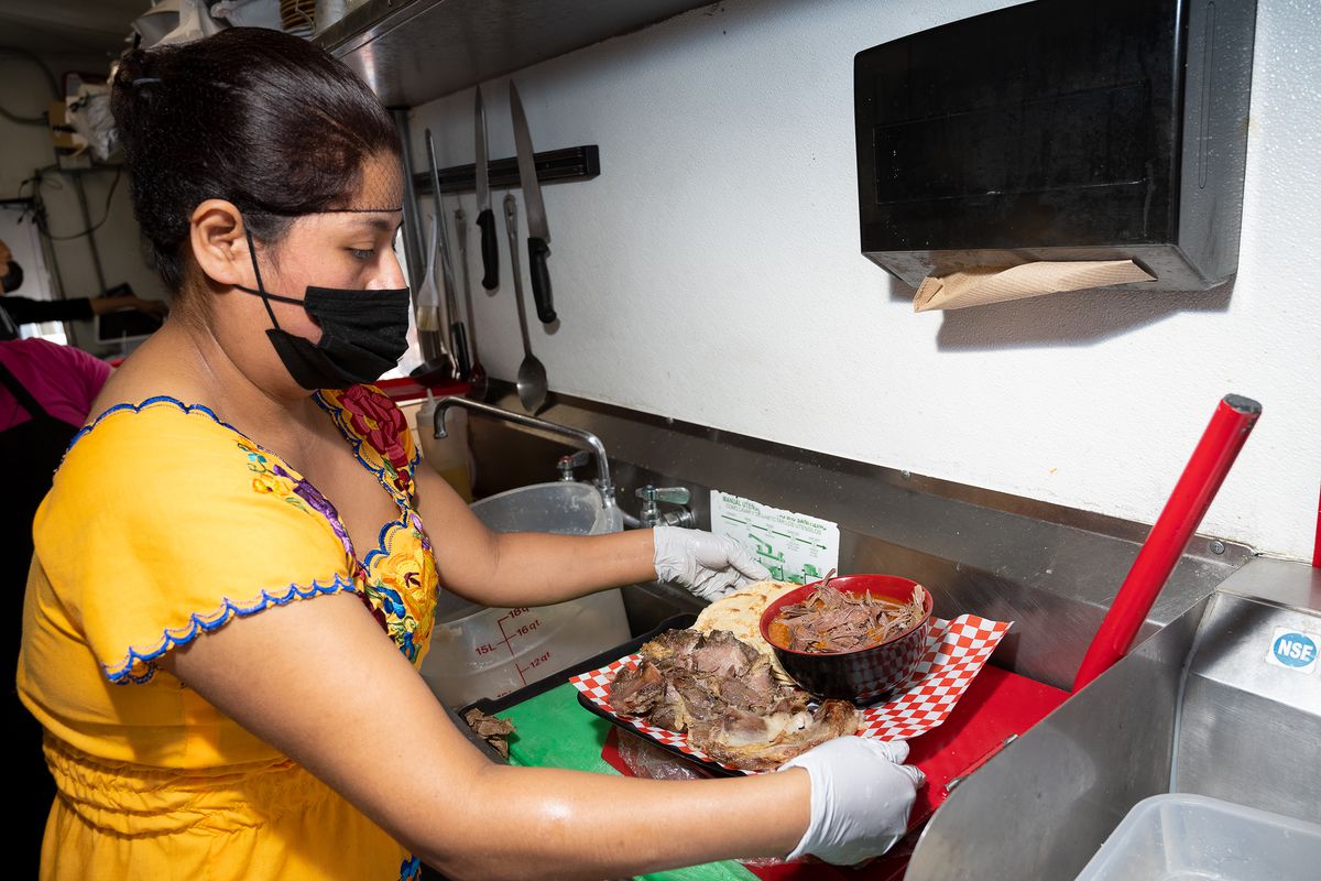 Faviella Cruz prepares masita with barbacoa on a tray lined with red-and-white checked paper.