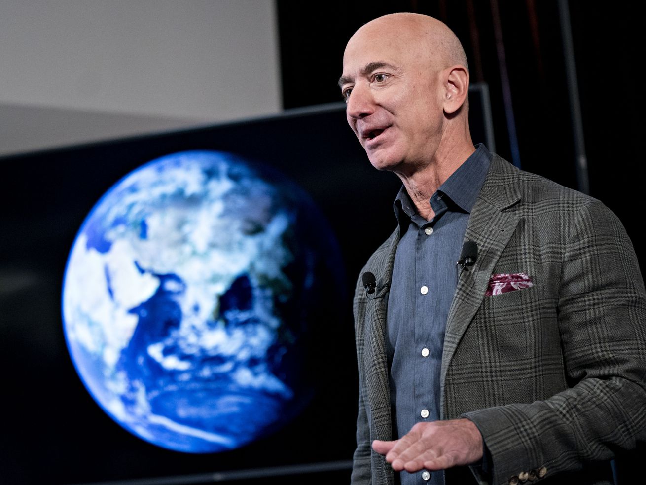 Jeff Bezos speaking onstage in front of a screen showing a picture of the Earth as seen from space.