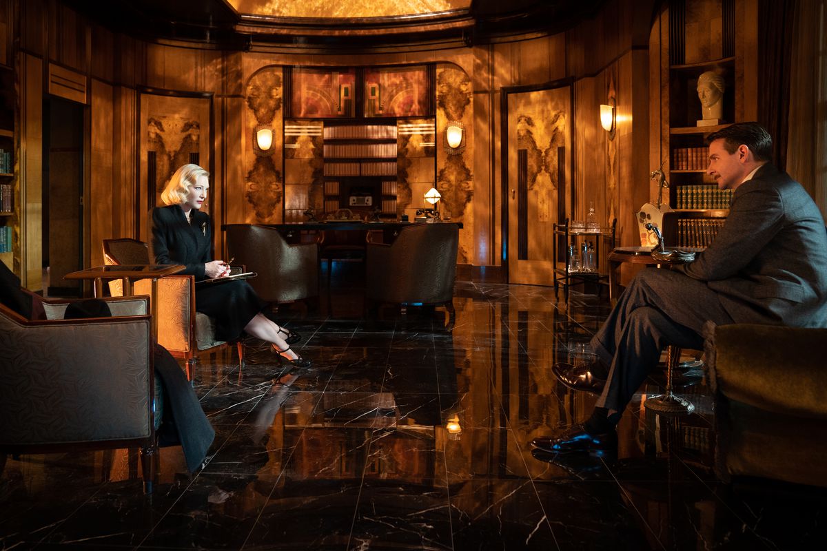 Stan Carlisle se sienta en la oficina art deco de la Dra. Lillith Ritter en Nightmare Alley de Guillermo del Toro.