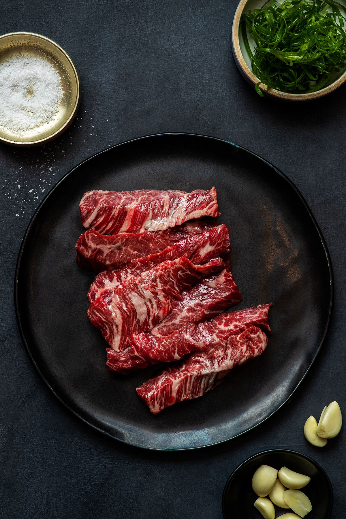 Several strips of highly marbled skirt steak on a black plate.