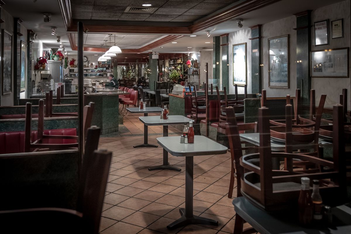 The interior of a closed diner, where chairs are overturned onto tables and bottles of ketchup, salt, and pepper are still propped onto tables