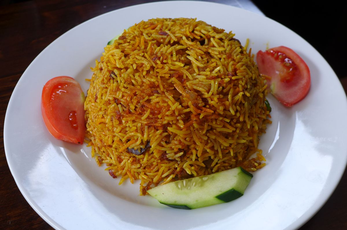 A mound of reddish rice with tomatoes and cucumber on the side.