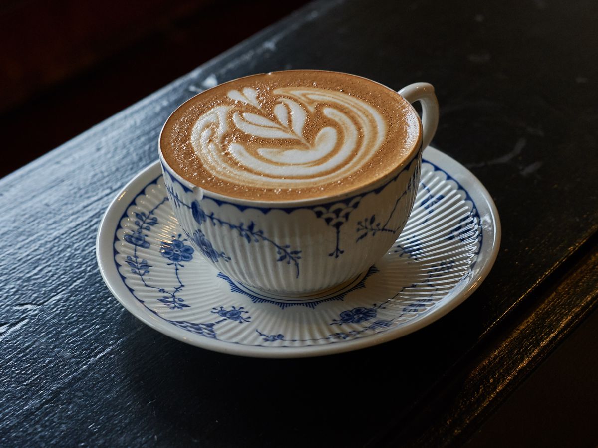 A latte with intricate foam art in a white and blue ceramic cup sitting on a dark wooden table.