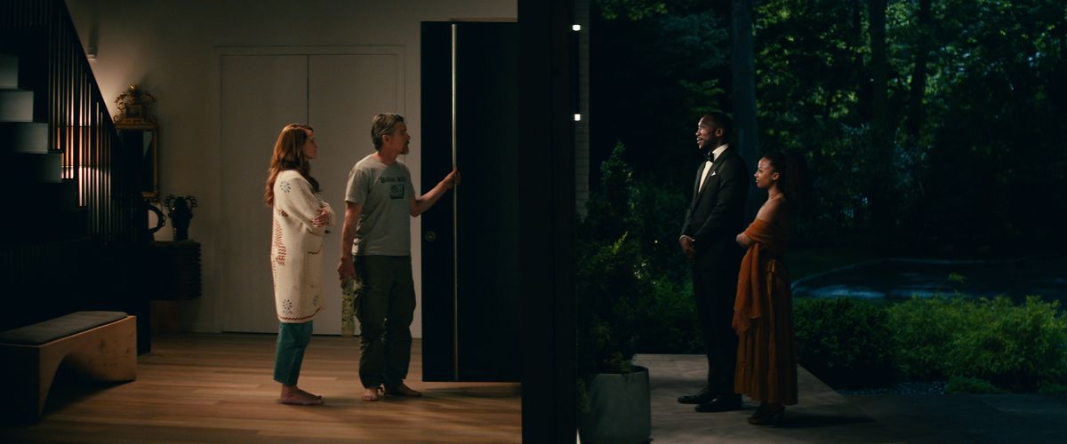 Julia Roberts and Ethan Hawke stand on one side of a split frame inside a lit hallway; on the other side, Mahershala Ali and Myha’la Herrold stand on a porch in the dark