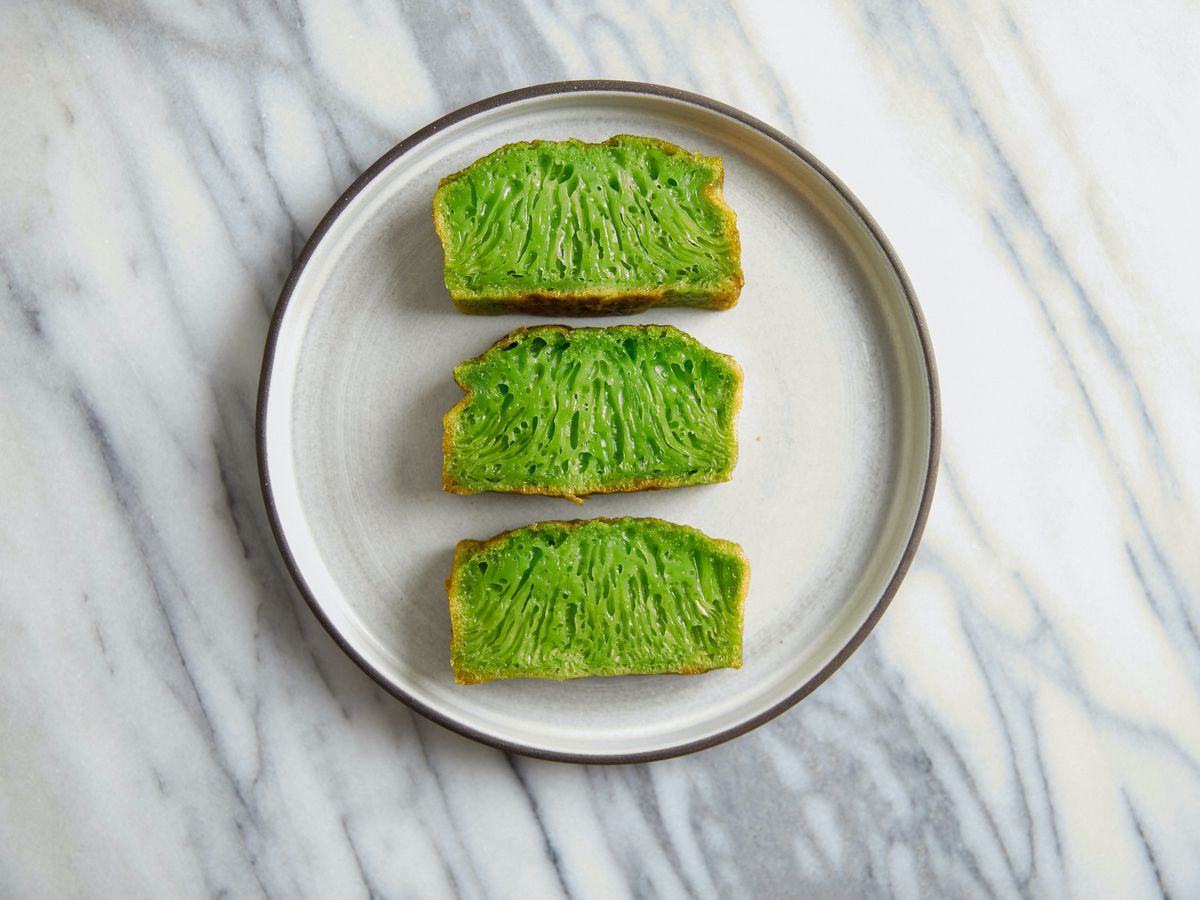 Three slices of bright green banh bo, a Vietnamese dessert, on a ceramic plate.