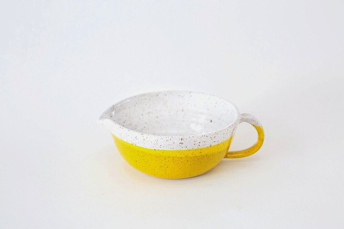 A yellow and white ceramic bowl with a spout and handle