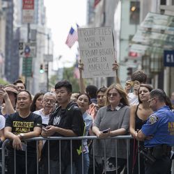 People including a protestor holding a sign line Fifth Avenue as they watch President Donald Trump's motorcade leave Trump Tower, Wednesday, Aug. 16, 2017, in New York. With corporate chieftains fleeing, President Donald Trump on Wednesday disbanded a pair of advisory business councils \_ the latest fallout from his comments on racially charged violence in Charlottesville.