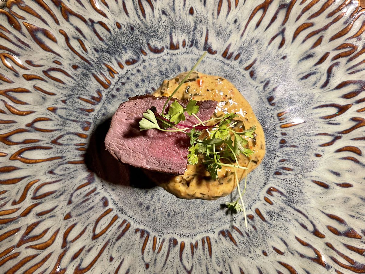 A plate with a venison and a dollop of red curry, topped with microgreens.