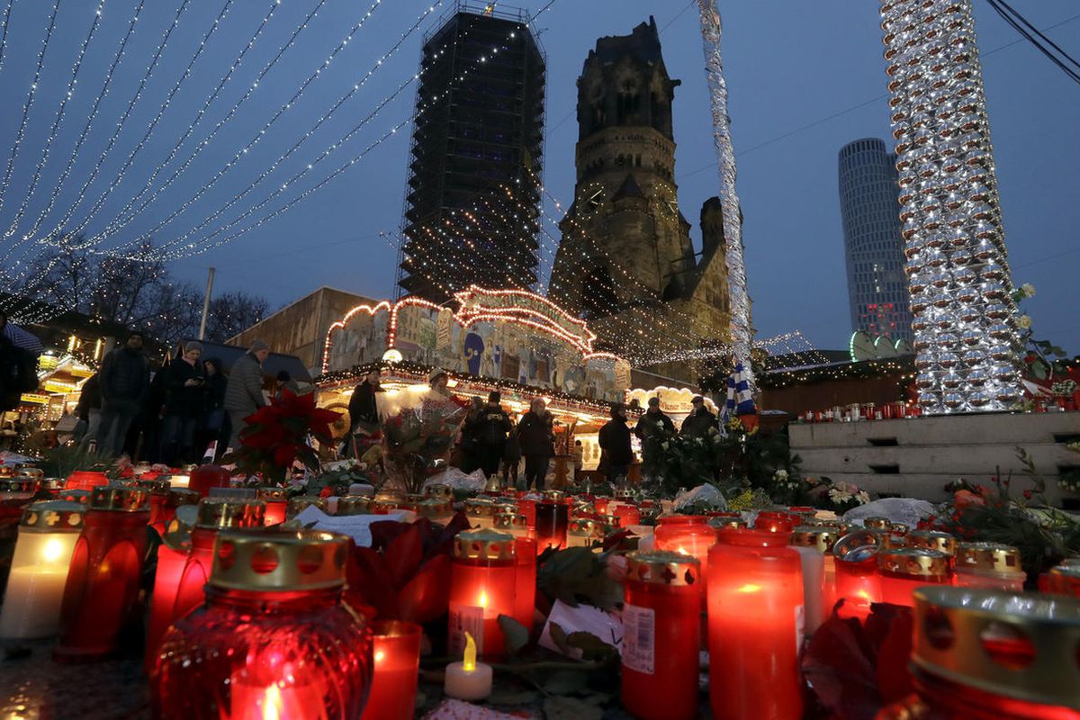 People walk past candles and flowers after the reopening of the Christmas market at the Kaiser Wilhelm Memorial Church in Berlin, Germany, Thursday, Dec. 22, 2016, three days after a truck ran into the crowded market and killed several people. (AP Photo/M