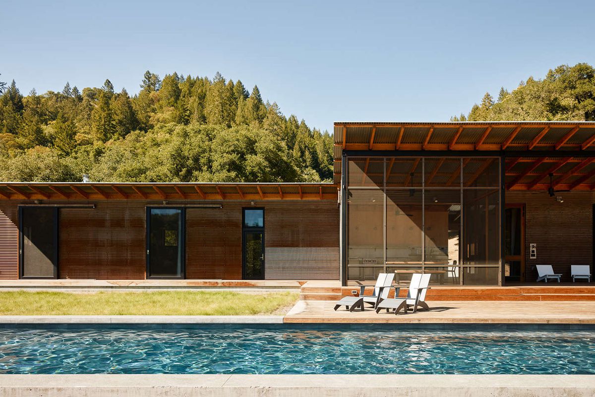 Exterior shot of steel-clad home with corrugated metal roof and long lap pool in front of it. 