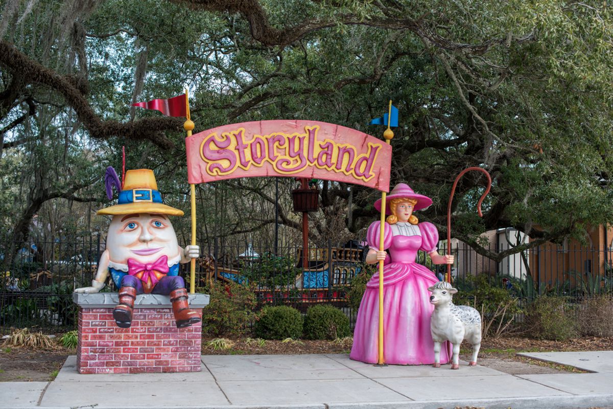 Two large fiberglass story tale characters stand in front of a tree-lined park
