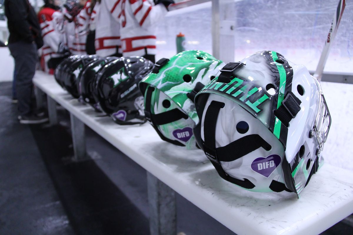 Helmets of the Markham Thunder sit on the bench with the green-and-white painted goalie helmets closest to the camera