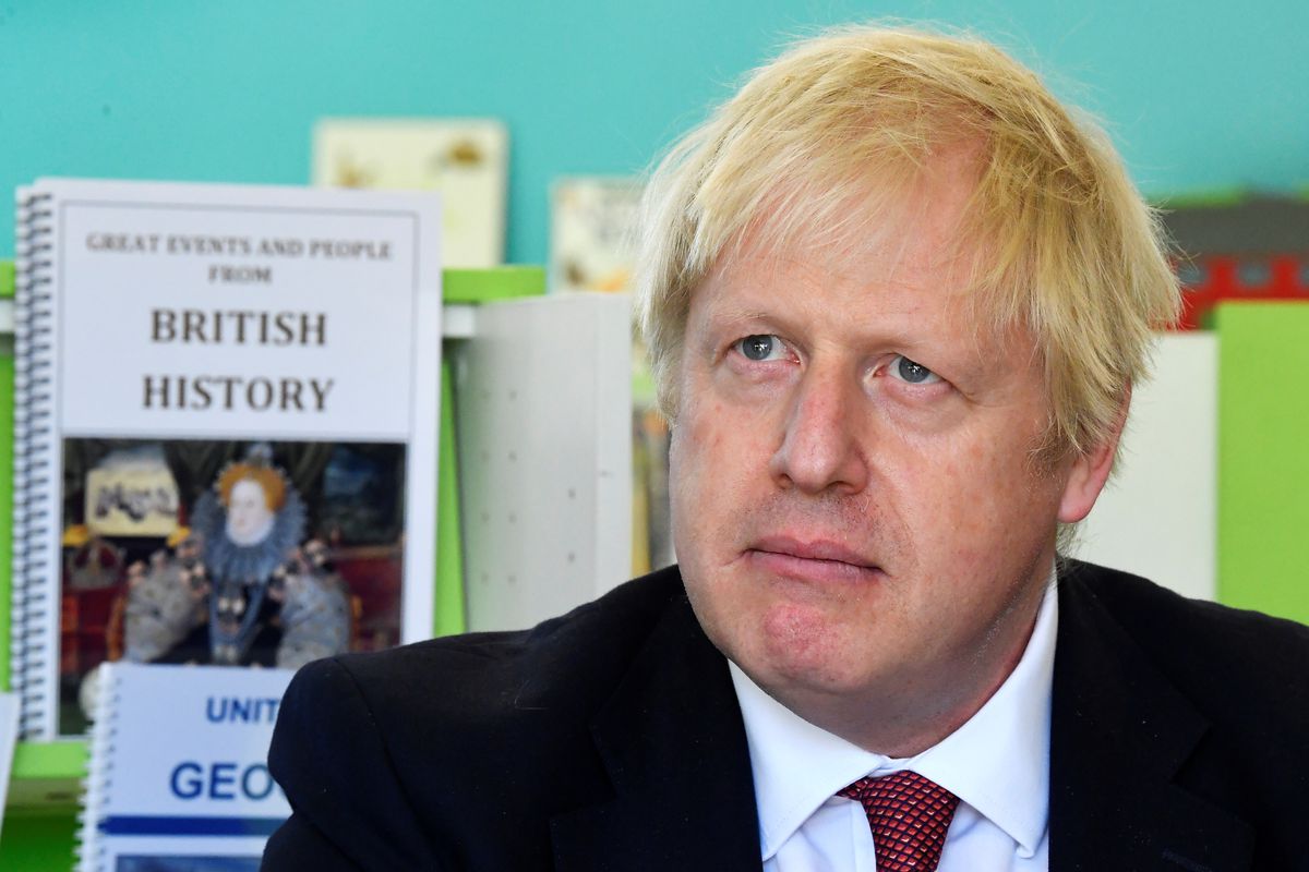 British Prime Minister Boris Johnson in a classroom with a British history textbook on a shelf behind him.