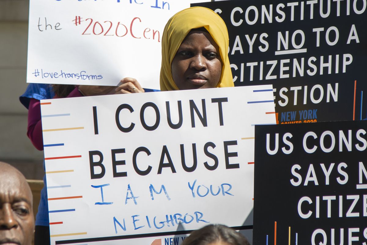 A black woman wearing a headscarf holds a poster that reads: “I count because I am your neighbor” and is surrounded by signs that say: “US Constitution Says No To Citizenship Question” during a press conference in NYC