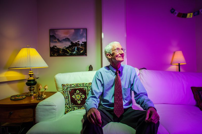 Roland R. Griffiths sitting on a white couch, half in yellow light and half in purple.