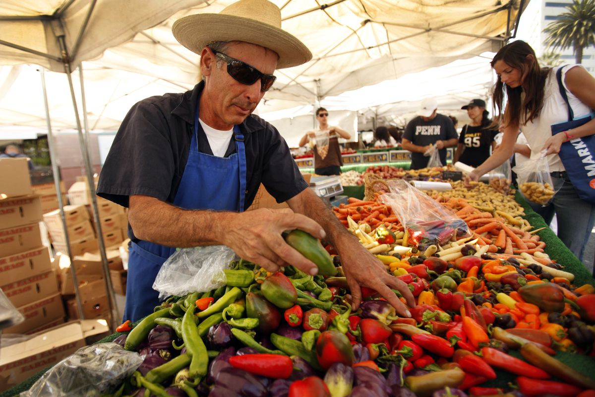 A vendor at a farmers market putting peppers on the table to sell.