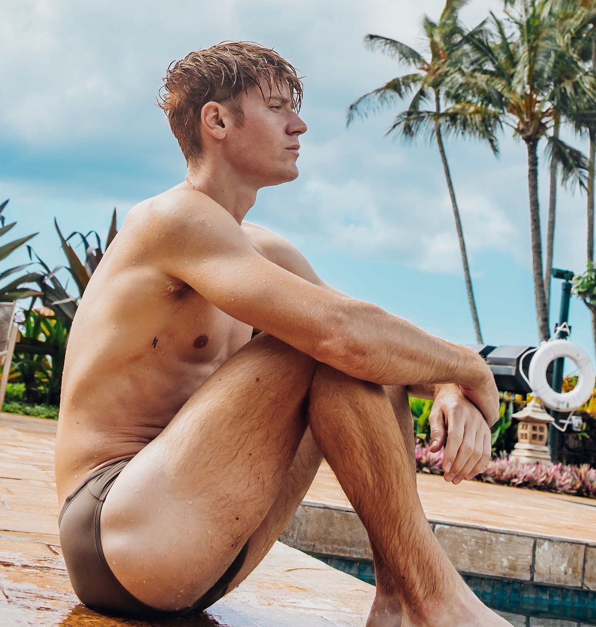 Zack Taylor sits by a pool in a swimsuit.