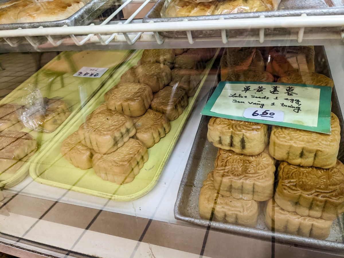Large, square mooncakes with an intricately decorated golden crust are on display in a pastry case.