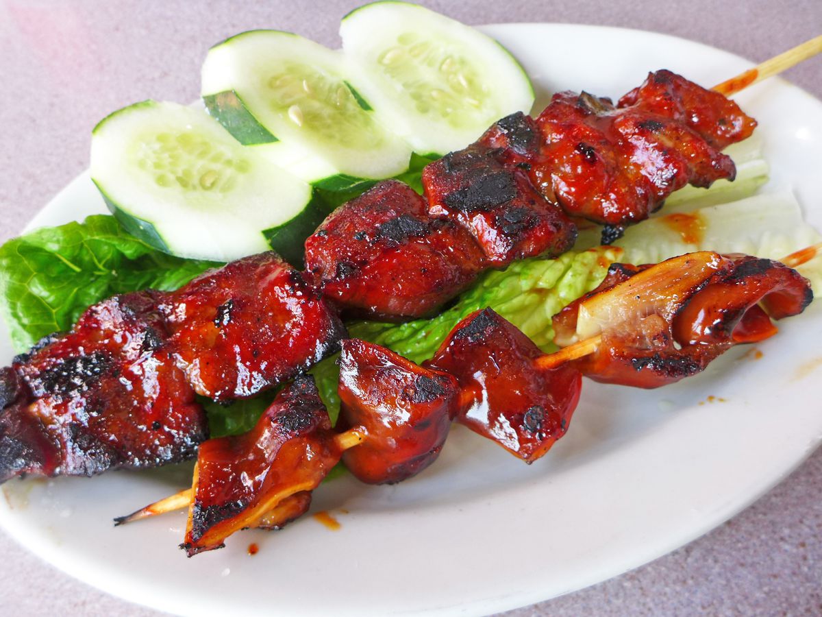 Two very red kebabs on a white plate with a row of cucumber slices.