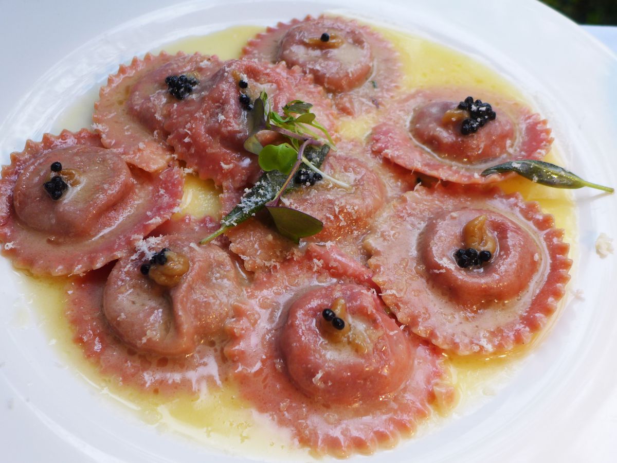 A shallow plate of red ravioli in yellow sauce.