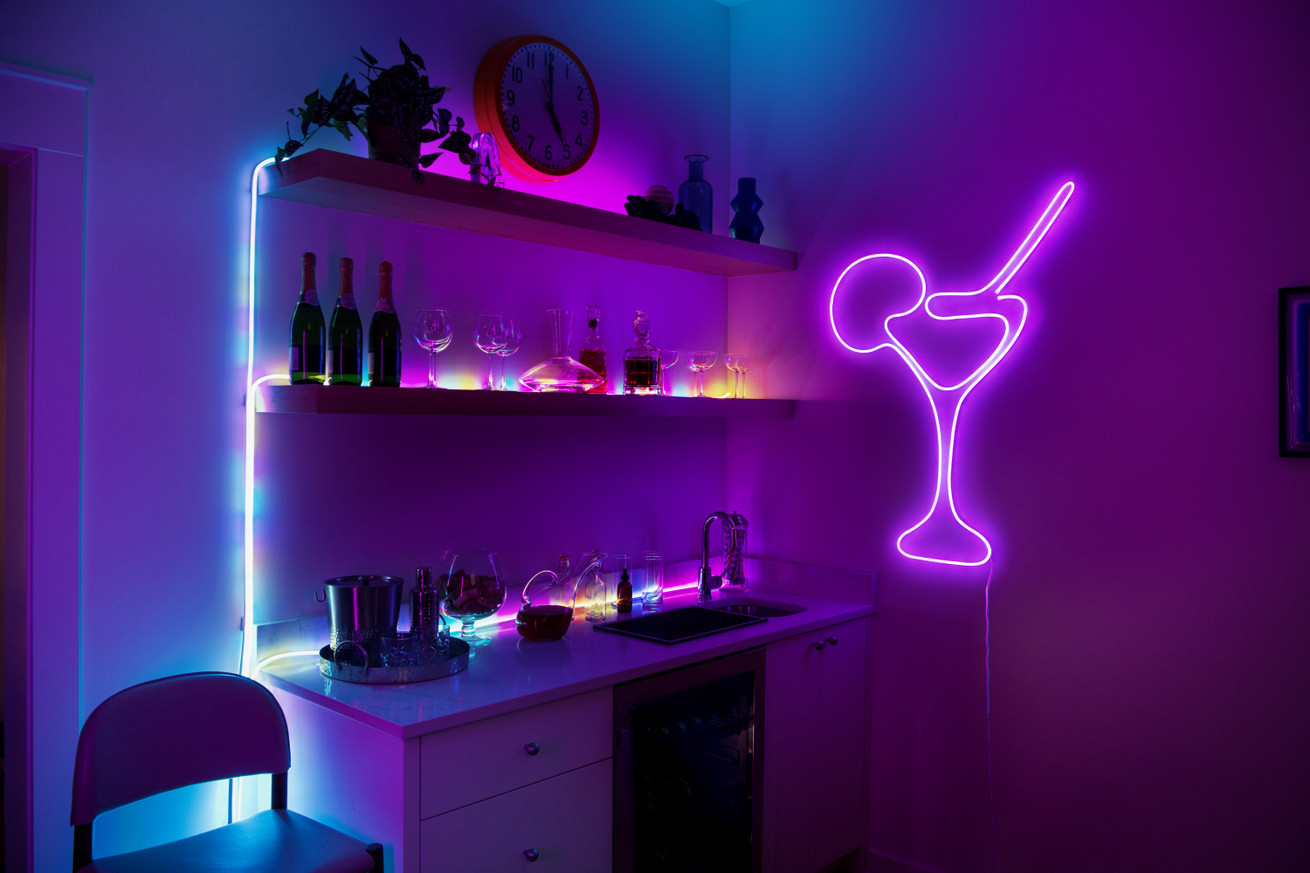 A neon rope light is used to create colorful backlights on shelves alongside the outline of a cocktail glass with straw and orange slice.