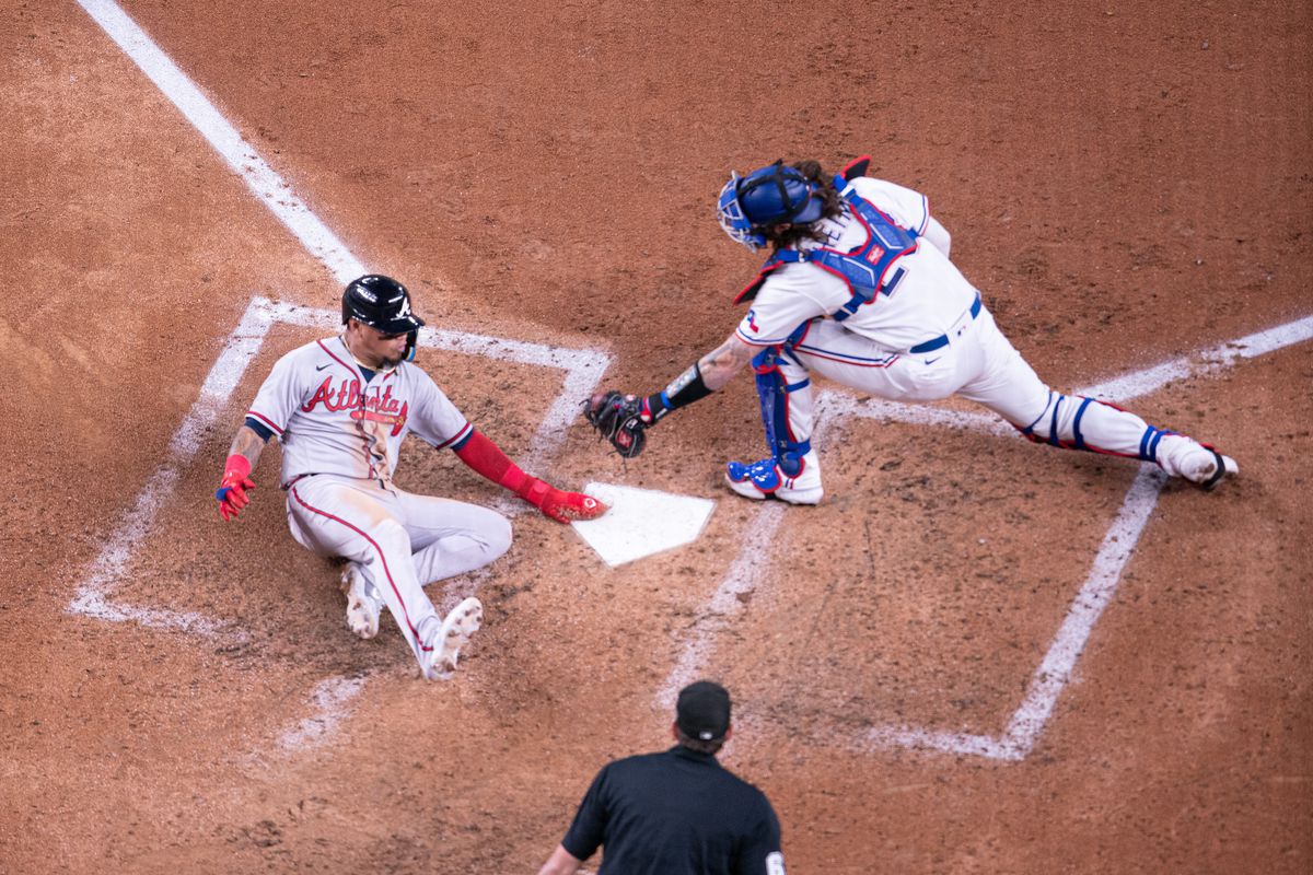 Atlanta Braves shortstop Orlando Arcia avoids the tag attempt by Texas Rangers catcher Jonah Heim during the fifth inning of a Major League Baseball game between the Atlanta Braves and the Texas Rangers on May 15, 2023, at Globe Life Park in Arlington TX.