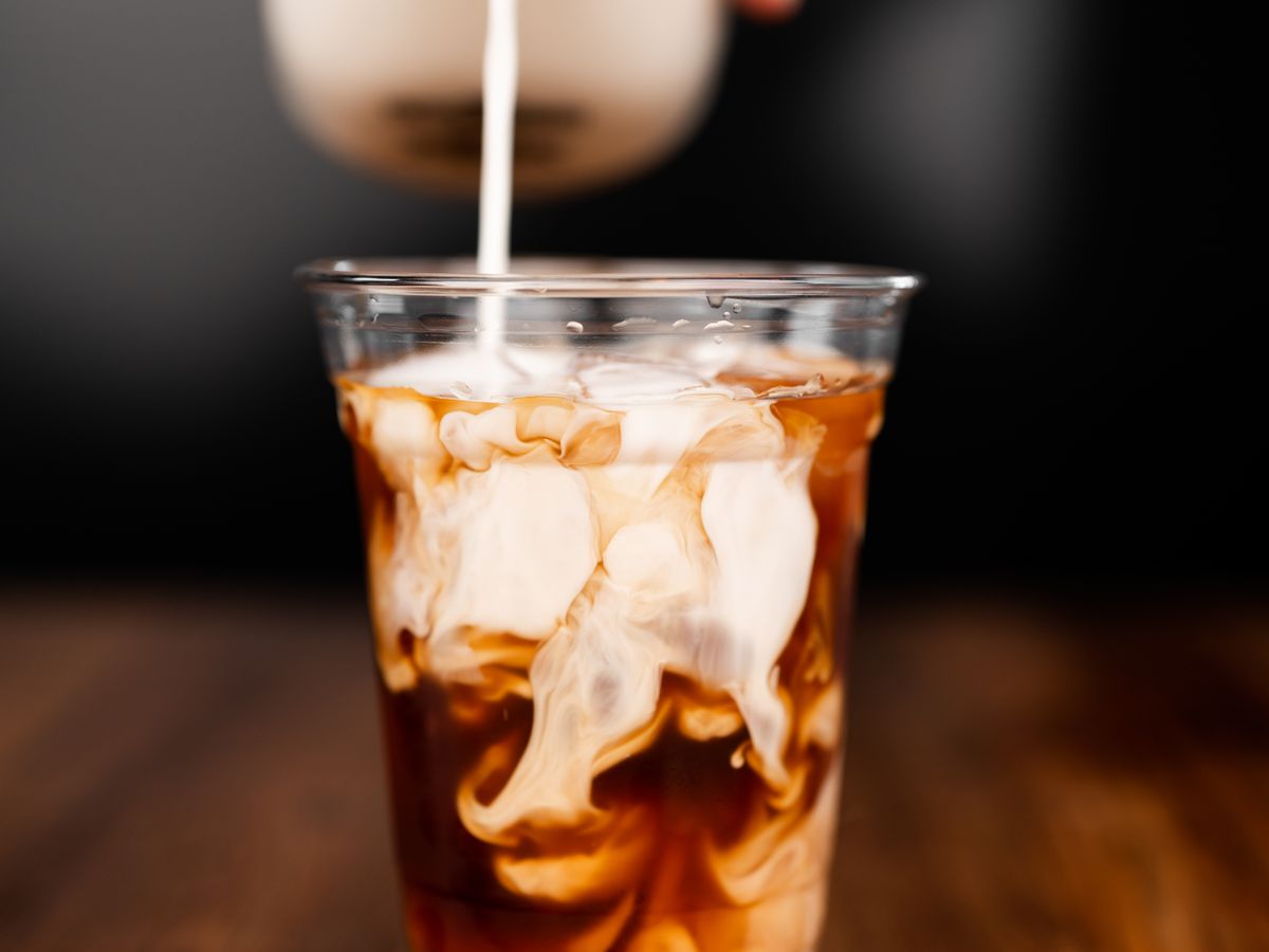 A hand pouring milk into a glass of cold brew coffee. 