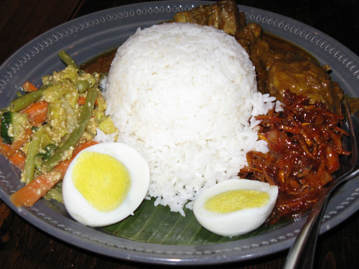 A Malaysian fish —&nbsp;curry chicken, rice, and a hard-boiled egg —&nbsp;on a banana leaf on a blue plate