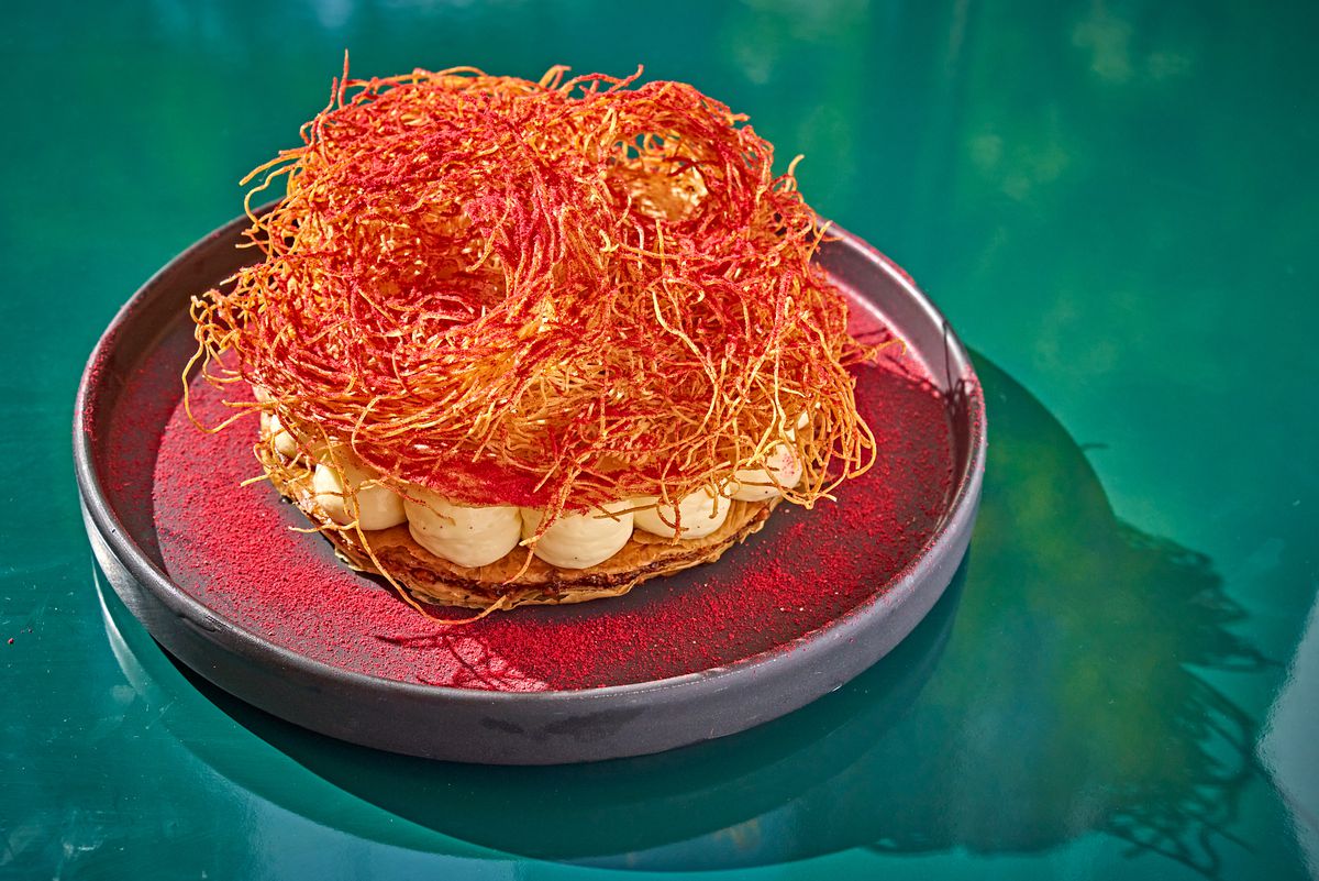 White cream cheese sits between layers of phyllo and underneath a red-tinted nest of kataifi