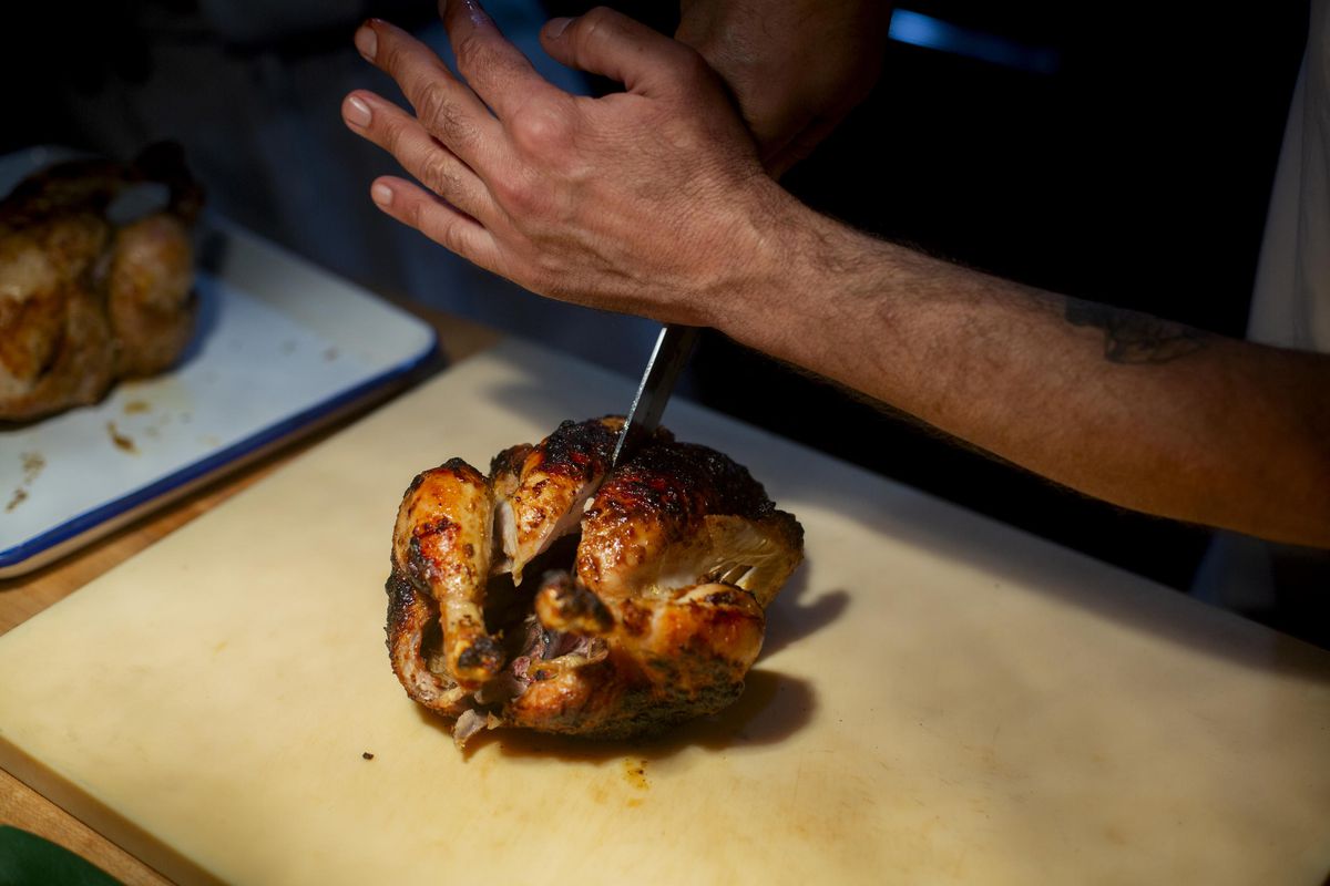 A knife cuts a roasted chicken.