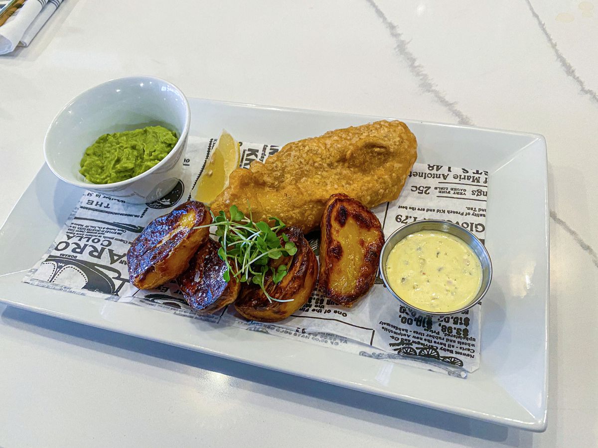 A fish and chips platter set on a white rectangular plate and newspaper print paper at Toria in Northville, Michigan.