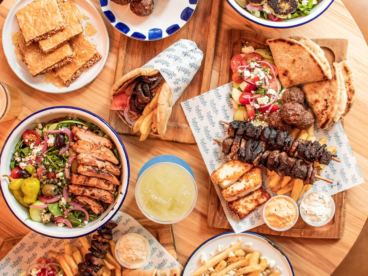 A spread of pita sandwiches, salads, and kabobs laid out on a circular wooden table.