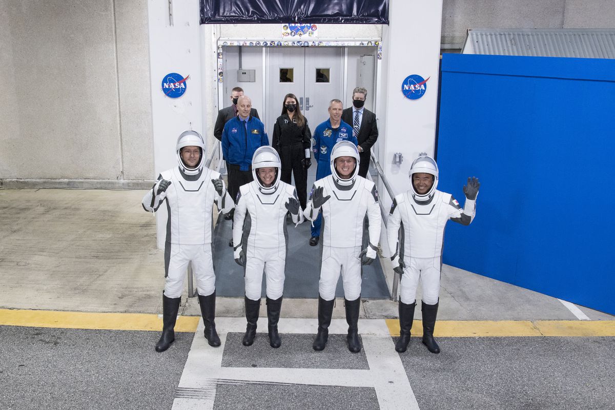 Dört astronot, uzay giysisi giymiş bir uzay gemisine binmek için yola çıkarken el sallıyor.