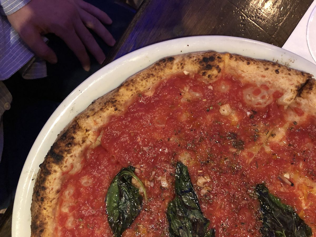Uncut marinara pizza at Don Antonio is garnished with three shriveled basil leaves and photographed from overhead.