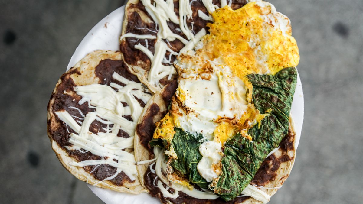 Cheese, bean, and egg-topped tacos on a paper plate.