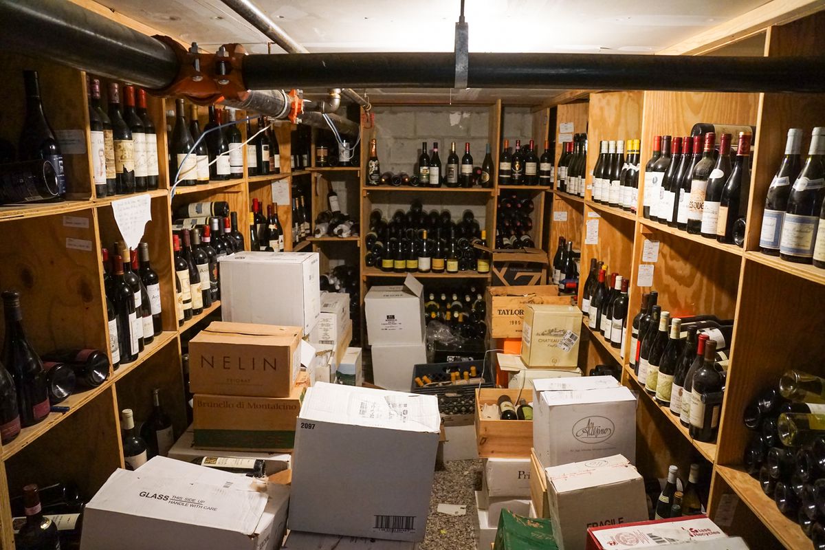 Boxes of wine and shelves bulging with bottles in an underground wine room.