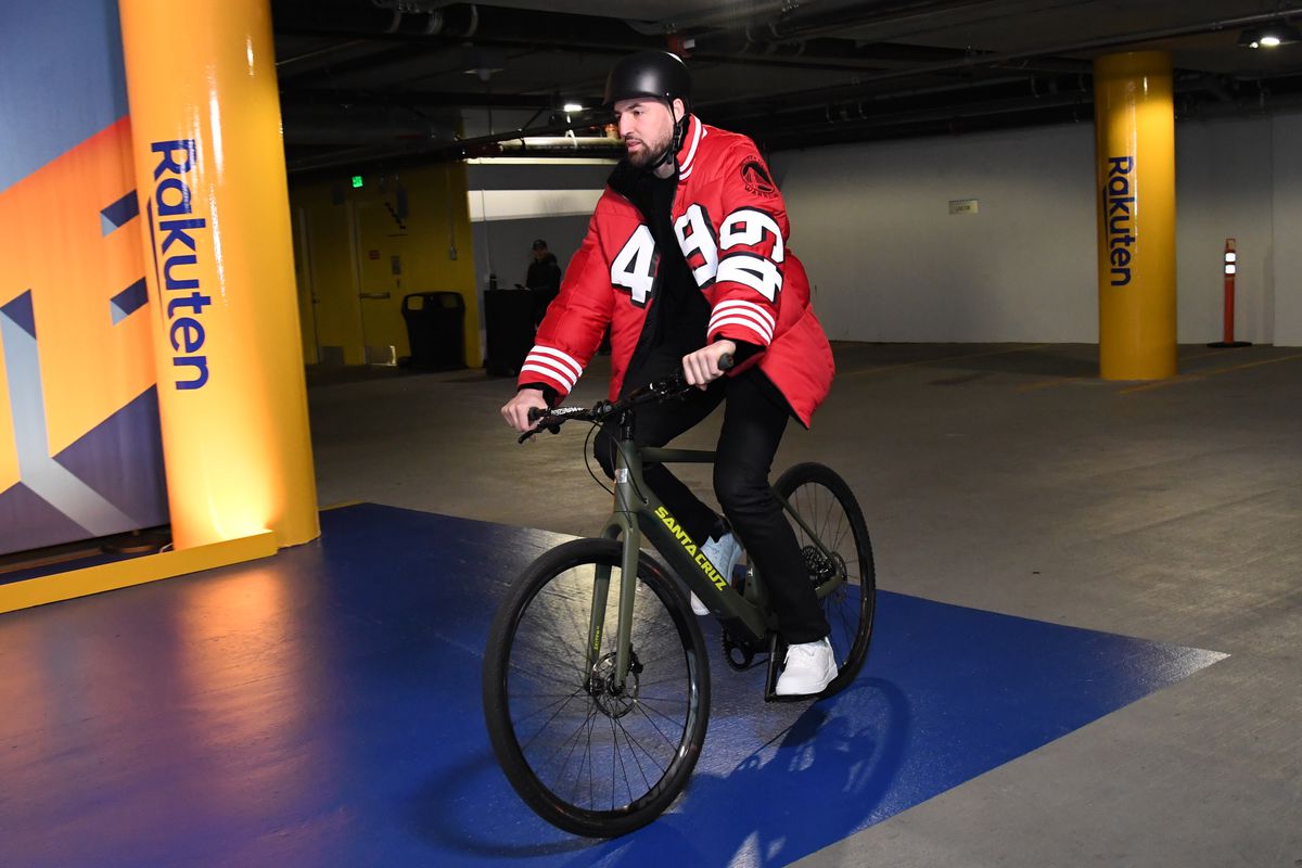 Klay Thompson riding a bicycle into the arena with a 49ers jacket on. 